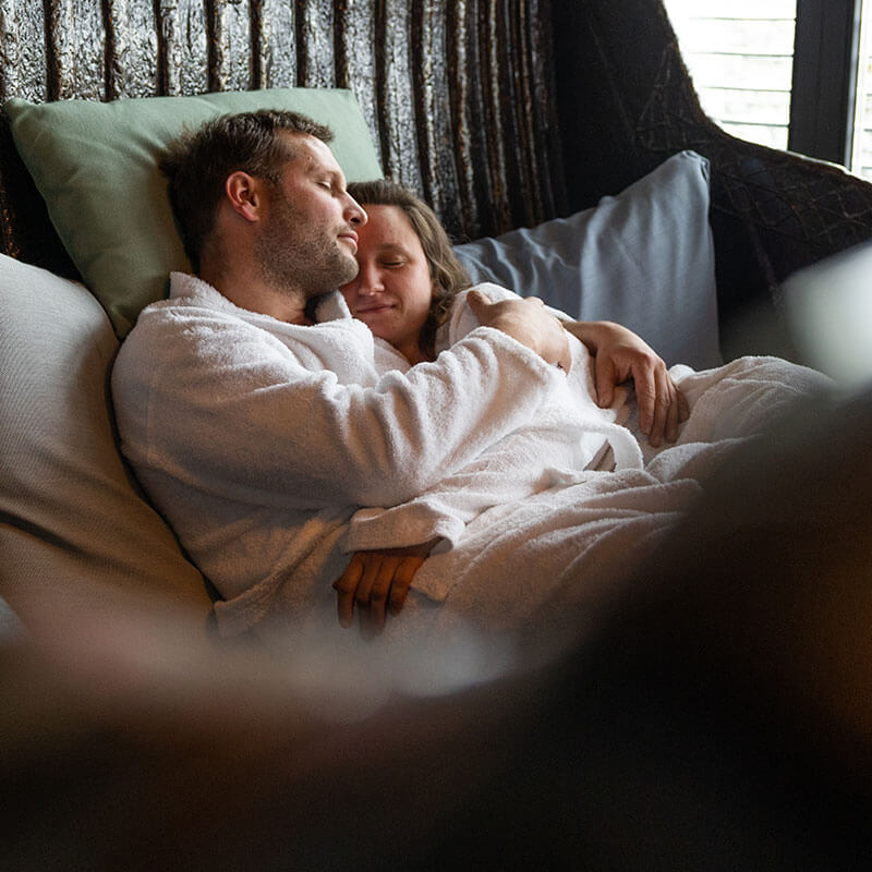 Ein Paar mit Bademänteln bekleidet in enger Umarmung in einem Wellnessbereich