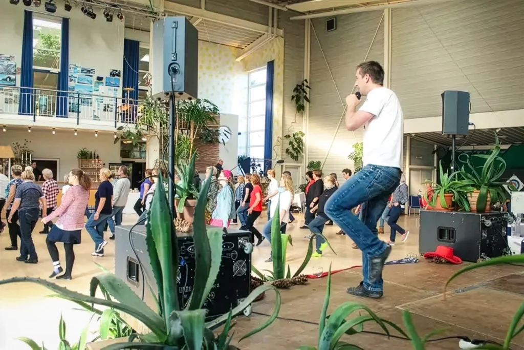Ein Tanztrainer auf einer Bühne koordiniert eine Tanzgruppe in einer großen Halle