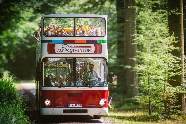 Ein Doppeldecker-Bus mit offenem Dach, in welchem eine Gruppe Menschen einen Ausflug ins Grüne macht