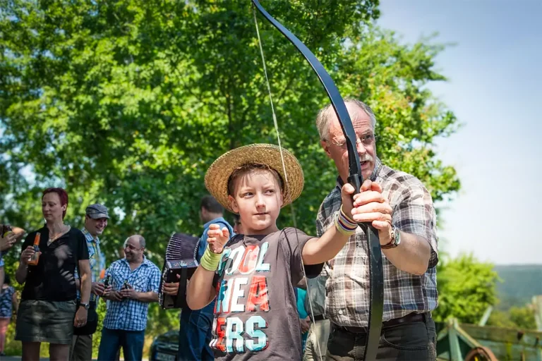 Ein Junge bekommt von einem älteren Mann gezeigt, wie er den Bogen zum Bogenschießen halten muss