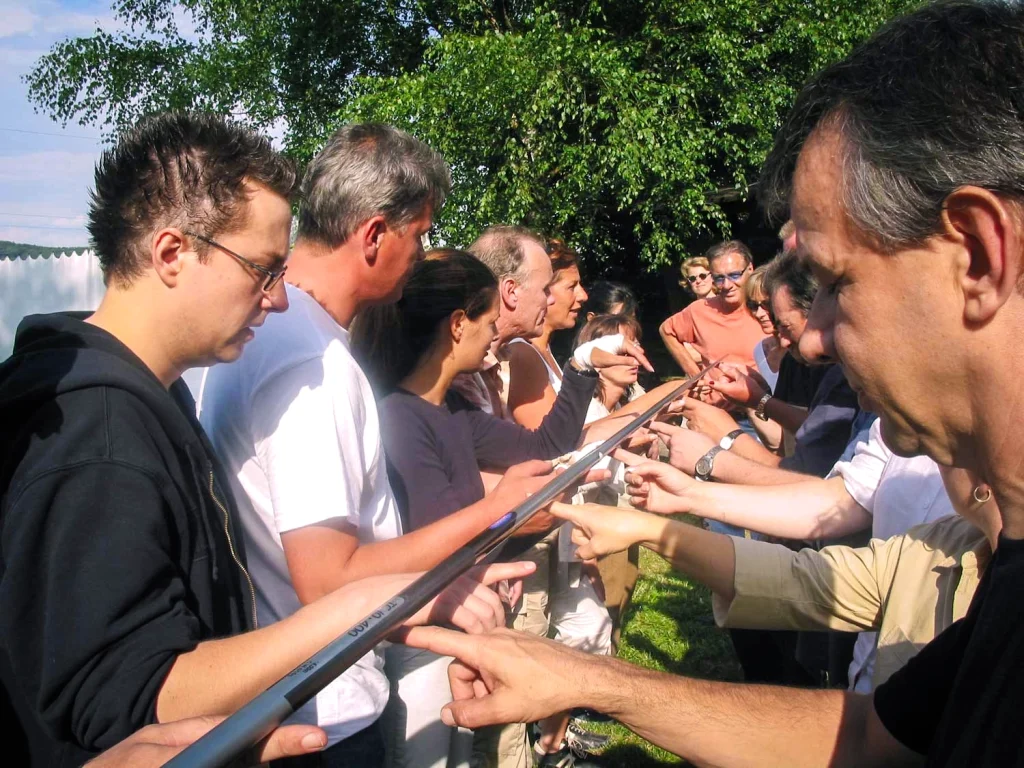 Eine Gruppe menschen balanciert gemeinsam einen Stab aus Metall auf den Händen