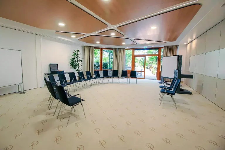 Tagungsraum mit halb geöffnetem Stuhlkreis, vor Kopf zwei Referentenstühle, Pinwänden und Moderationsmaterial