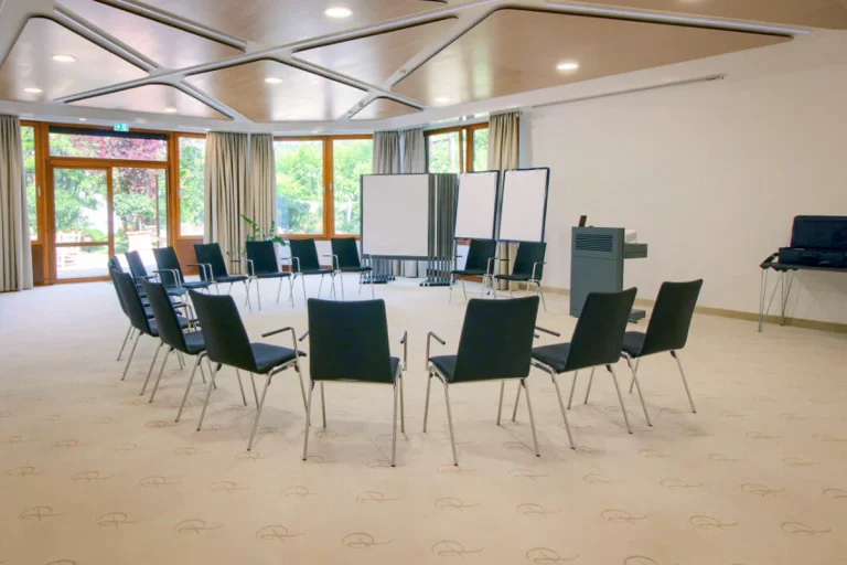 Tagungsraum mit halb geöffnetem Stuhlkreis, vor Kopf zwei Referentenstühle, Pinwände und Moderationsmaterial