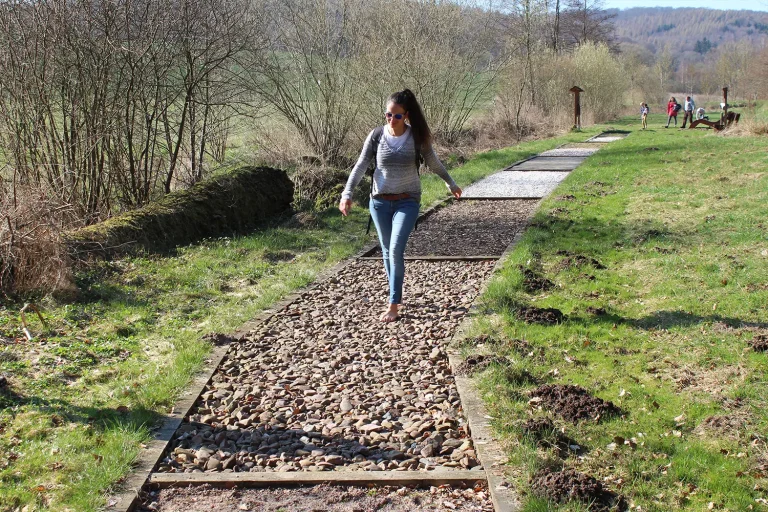 Eine Frau wandert barfuß über einen Barfußpfad mit Kieselsteinen