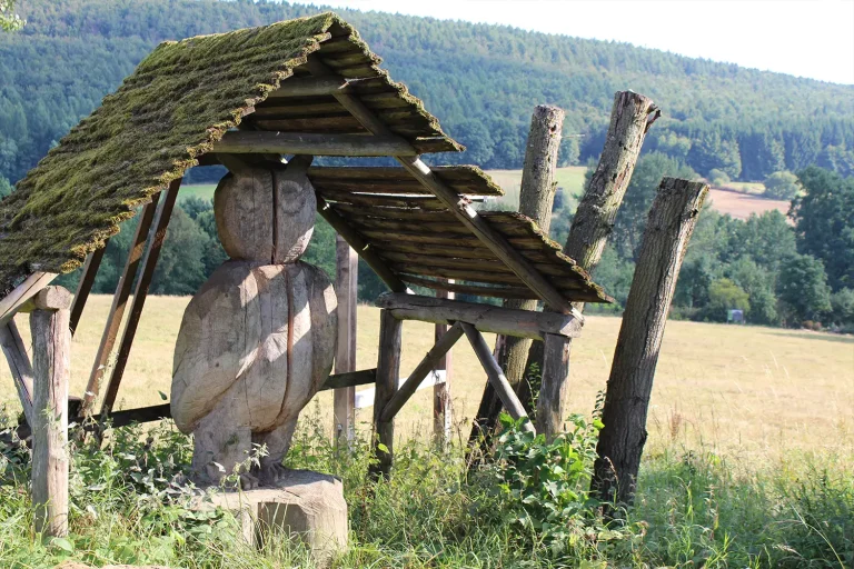 Eine Eule aus Holz unter einem Holzdach am Feldrand