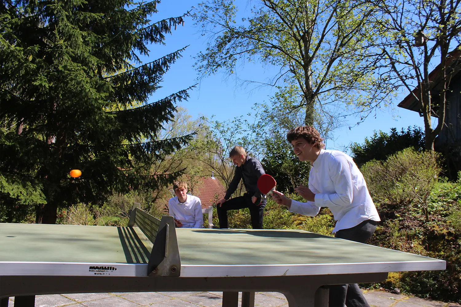 Drei Jungs spielen an einer Tischtennis-Platte im Freien