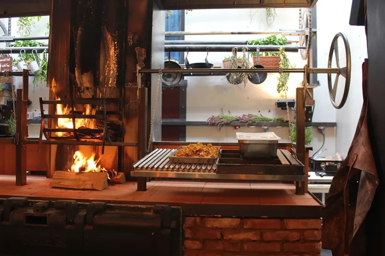 Offene Küche mit getrockneten Kräutern, gusseinsernen Pfannen und einem Holzgrill, auf dem bereits das Feuer entzündet wurde