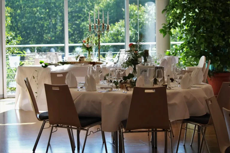 Festlich gedeckte runde Tische vor einer großen Fensterfront mit Blick ins Grüne