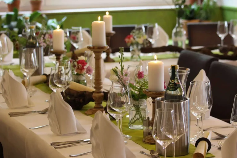 festlich geschmückter Tisch im Restaurant mit Servietten, Weingläsern, Kerzen und Wasserkühler