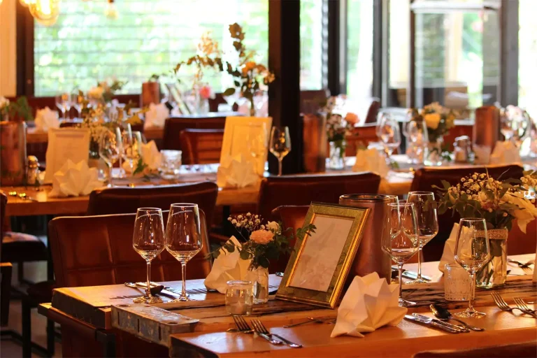 festlich geschmückte und eingedeckte Tische mit Weingläsern, Stoffservietten und Tischaufstellern in einem Restaurant