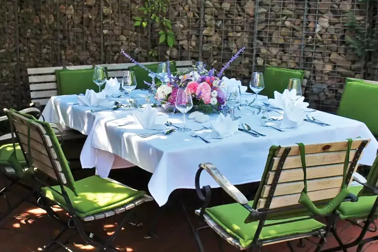ein stimmungsvoll mit Blumendekoration eingedeckter Tisch im Garten vor einer Gabionenmauer