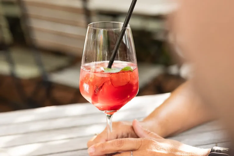 Ein roter Cocktail mit Eiswürfeln und einem grünen Blatt in einem großen Weinglas mit Strohhalm