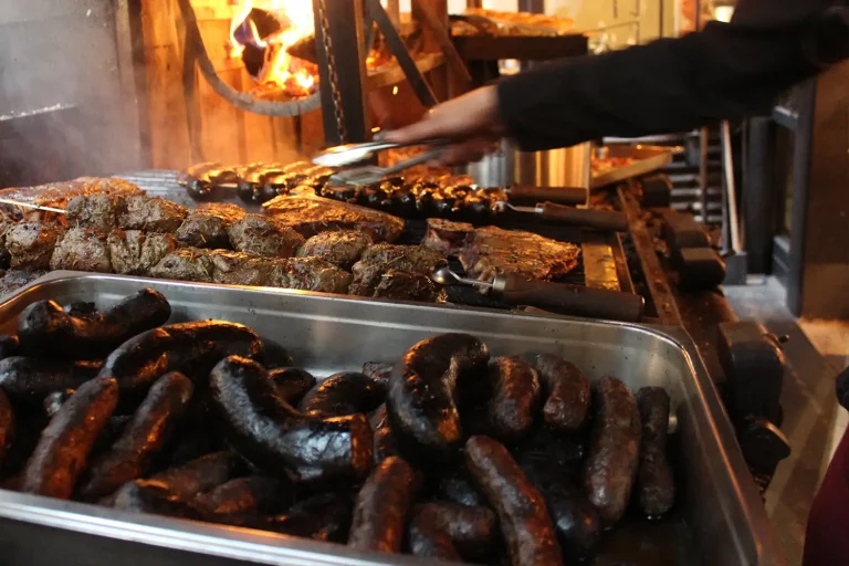 verschiedene Grillspezialitäten wie dunkle Würste und Fleischspieße, die zum Grillen bereitstehen