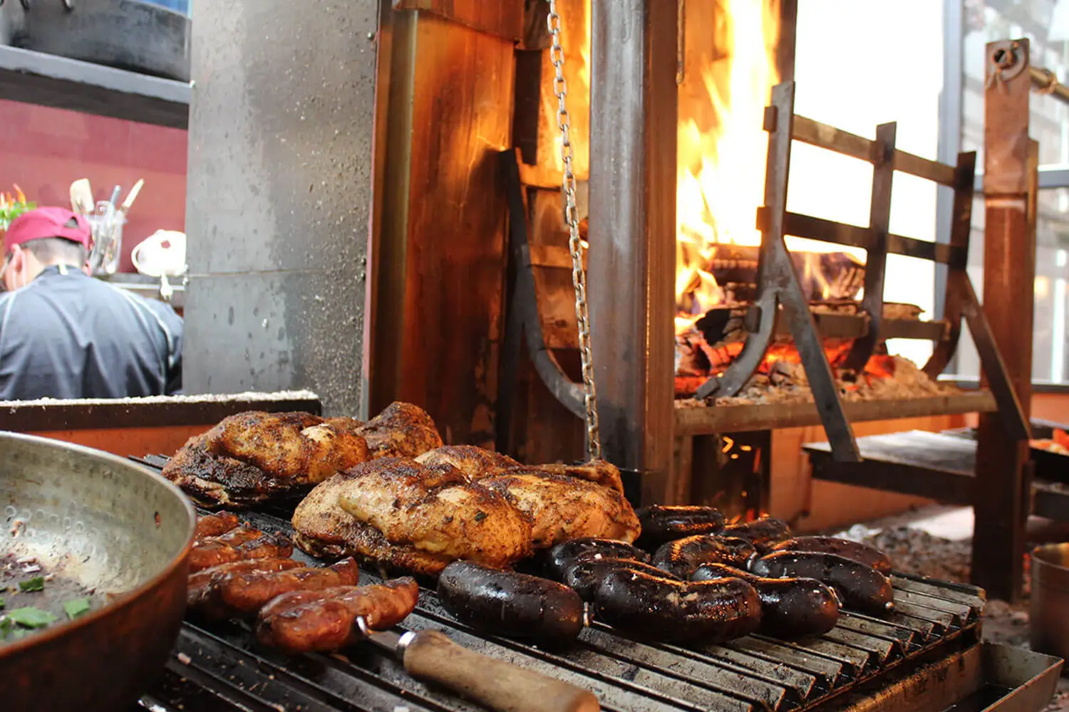 Verschiedene Grillspezialitäten wie Würste und Fleischspieße, die zum Grillen neben einem Grill mit Holzfeuer liegen.