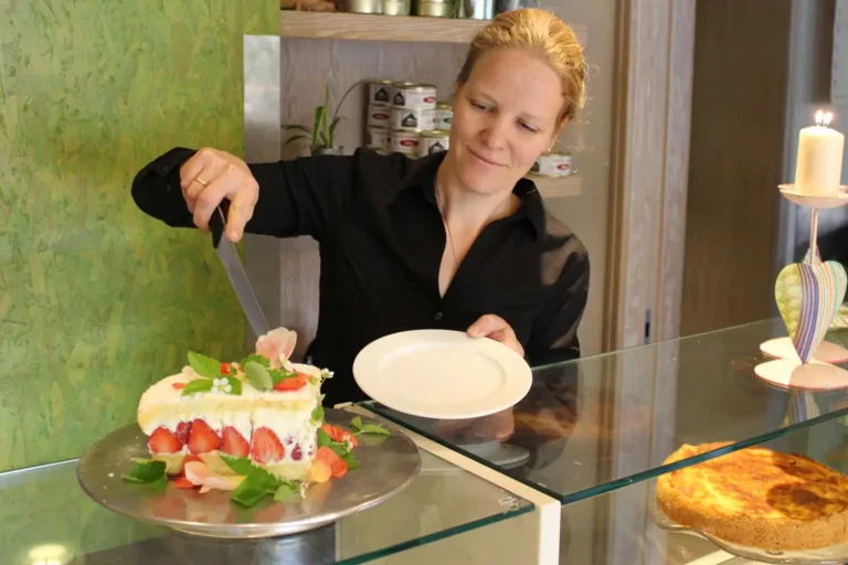 Eine Frau schneidet ein Stück aus einer schön verzierten Erdbeertorte, um es auf einem Teller zu servieren