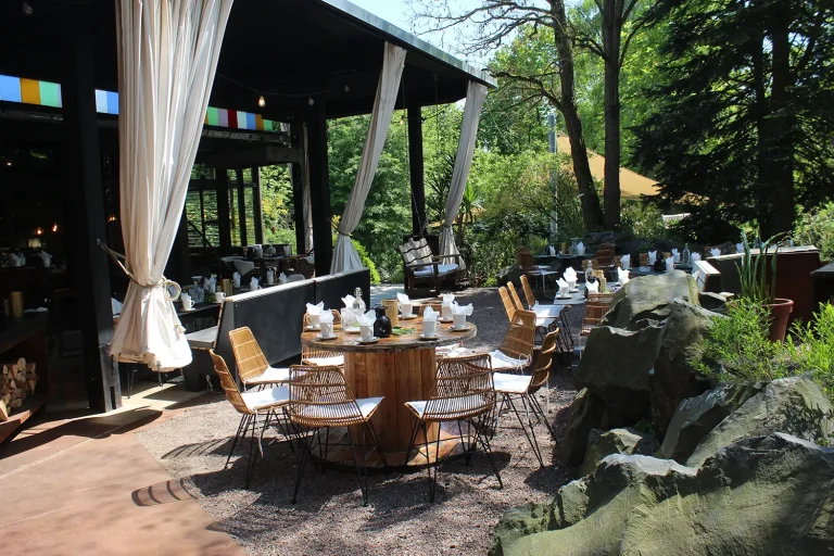 Terrasse mit überdachten und nicht überdachten Bereichen in einer üppig bepflanzten Umgebung mit vielen rustikalen Sitzgelegenheiten