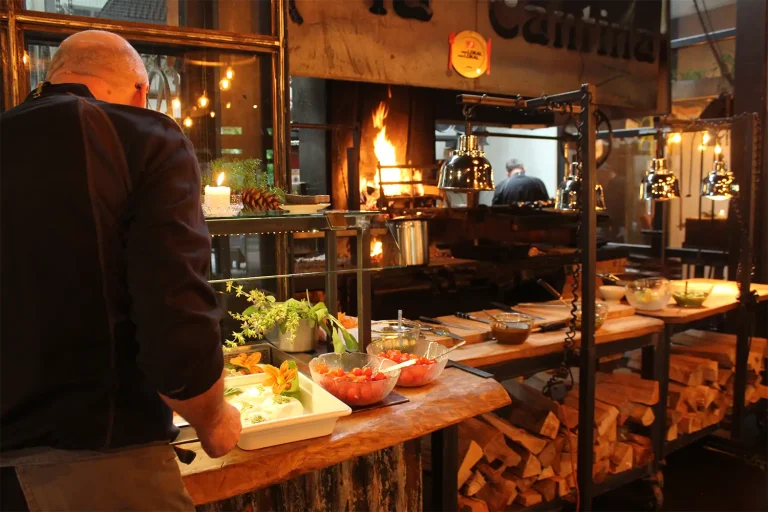 offene Küche mit Holzfeuer, in der gerade von einem Koch Vorbereitungen für ein Buffet getroffen werden