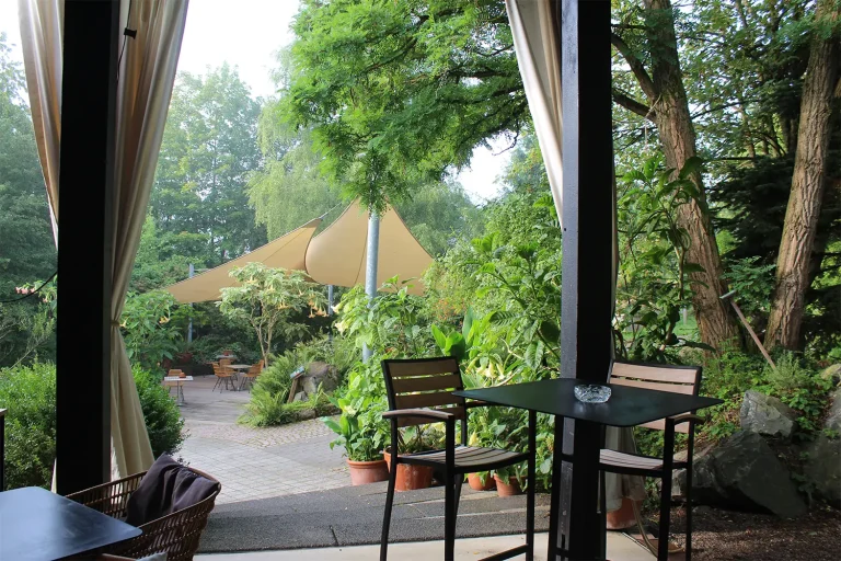 Von einer überdachten Terrasse führt eine Steintreppe in eine grüne Gartenanlage