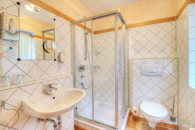 Helles Badezimmer mit weißen Kachel-Fliesen, Waschbecken, Dusche und Toilette