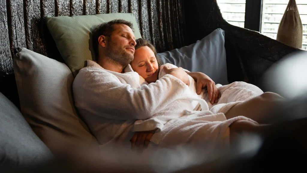 Ein Paar in Bademänteln liegt gemeinsam mit geschlossenen Augen und in entspannter Atmosphäre auf einem Kissen