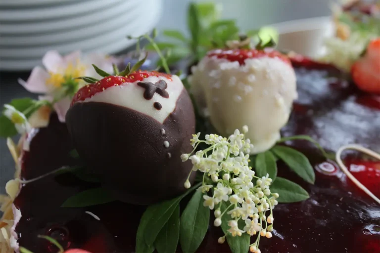 Zwei Erdbeeren, die mit Schokolade so verziert sind, dass sie an ein Brautpaar erinnern