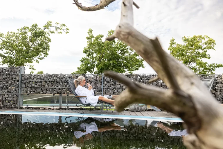 Eine Frau sitzt im Bademantel auf einer weißen Liege an einem Wasserbecken