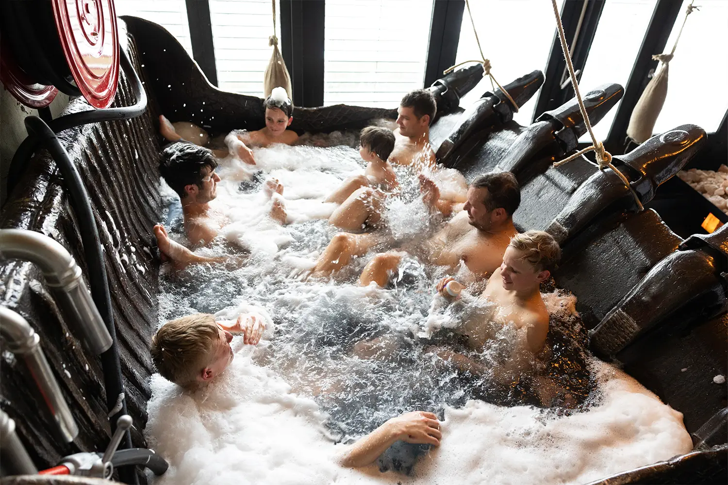 Eine Gruppe Männer und Jungen badet gemeinsam in einer großen Baggerschaufel, die zu einer Badewanne umfunktioniert wurde