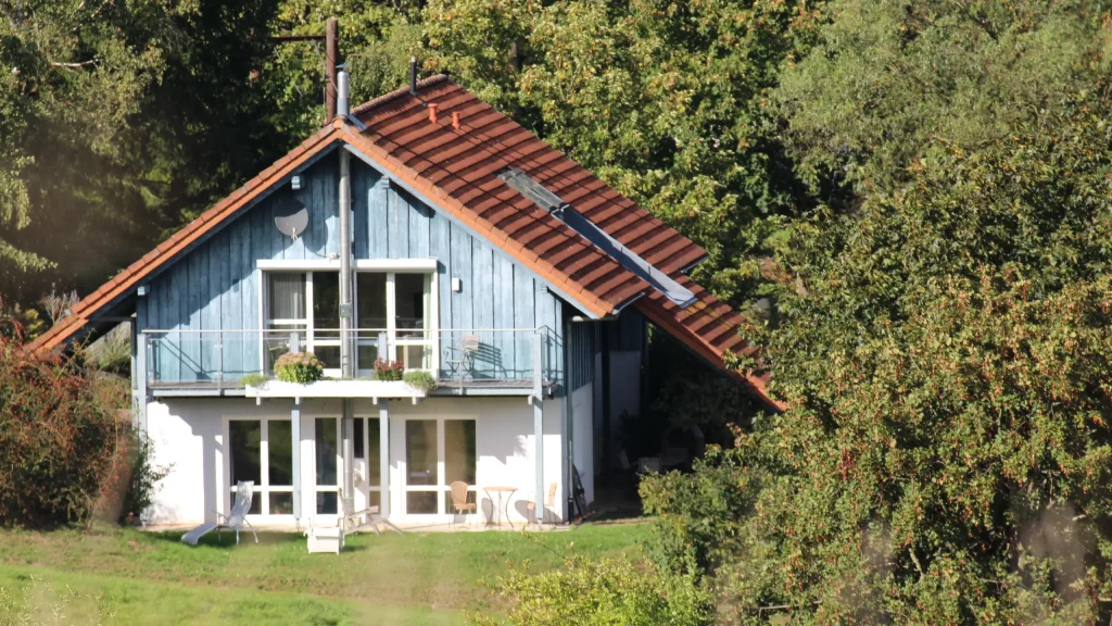 Rückseite eines zweistöckigen Hauses mit Balkon und Terrasse mitten im Grünen