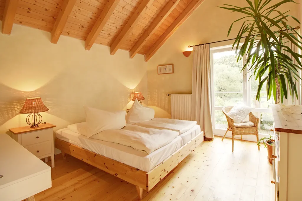 Großes Zimmer mit Dachschräge, Doppelbett und großer Fensterfront