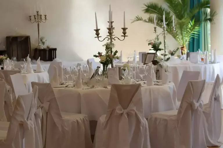 Festlich weiß geschmückter runder Tisch mit Stuhlhussen und großem Kerzenleuchter in der Mitte