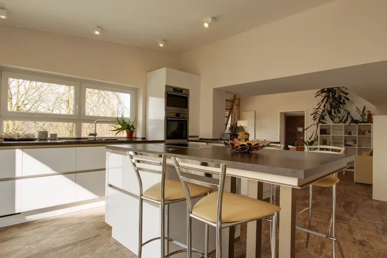 Moderne weiße Küche mit hohem Esstisch in der Mitte und vier hohen Stühlen