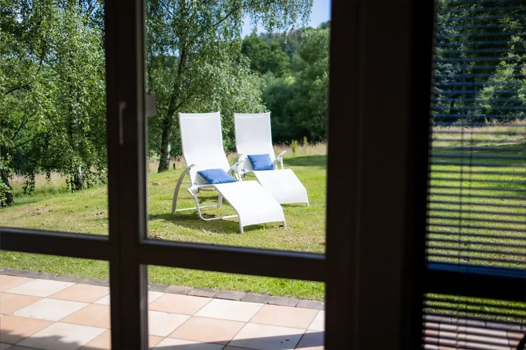 Zwei weiße Gartenliegen mit blauen Kissen auf einer grünen Wiese