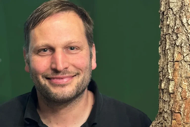 Ein Mann mit schwarzem T-Shirt vor einer grünen Wand