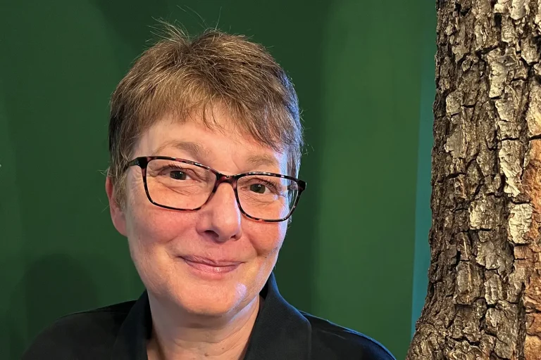 Eine kurzhaarige Frau mit Brille vor einer grünen Wand