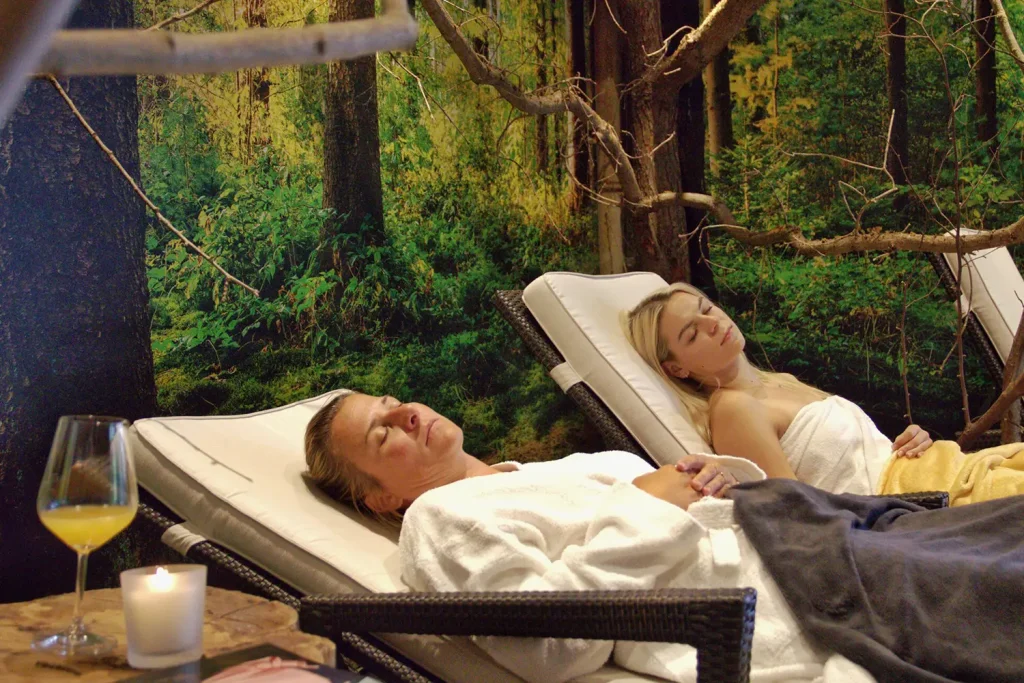 Zwei Frau liegen in Bademantel und Handtücher gekleidet auf einer Liege und entspannen