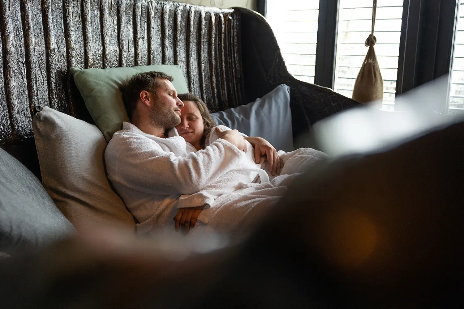 Ein Mann und eine Frau in inniger Umarmung entspannen in Bademänteln in einer großen Wanne liegend