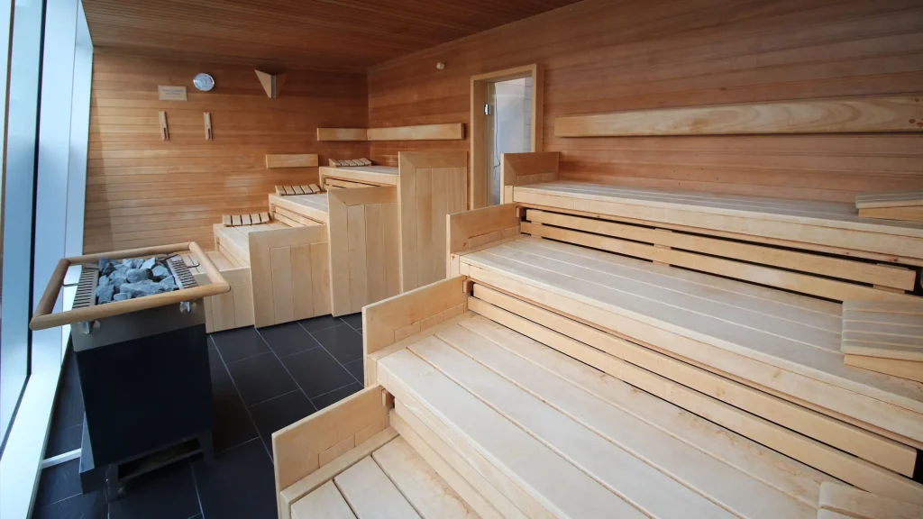 Großer Sauna-Raum mit acht Holzbänken, stufenweise jeweils vier übereinander angelegt und einem Steinofen in der Mitte