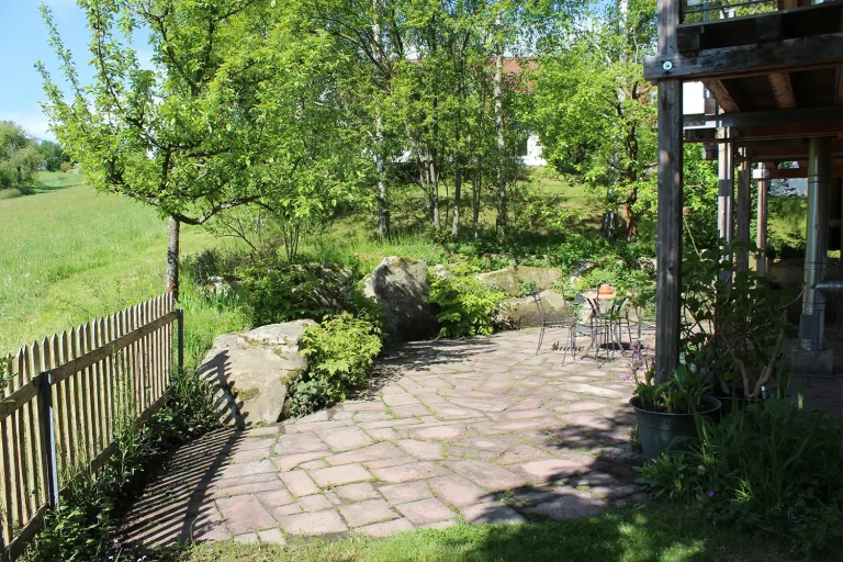 Steinterrasse mit Sitzgelegnheit angrenzend an eine grüne Wiese