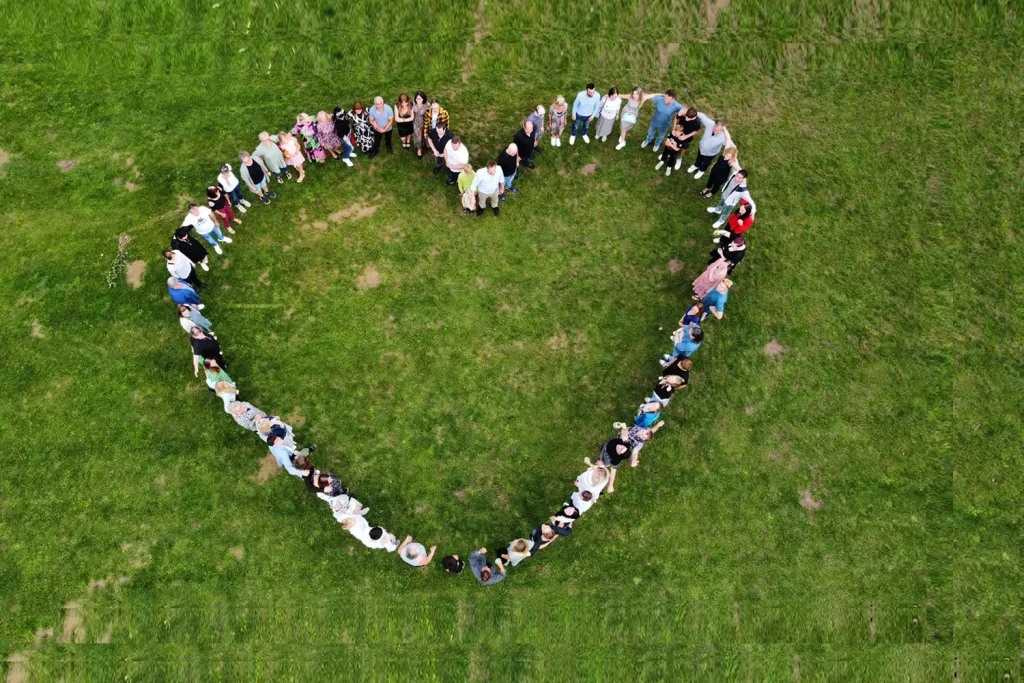 Menschen auf einer grünen Wiese, die sich in einer Herzform aufgestellt haben.