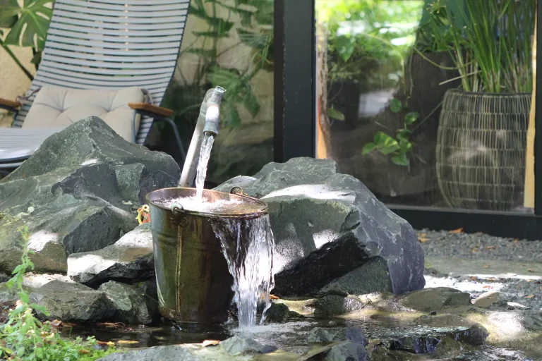 Aus einem Metallwasserschlauch fließt Wasser in einen Metalleimer