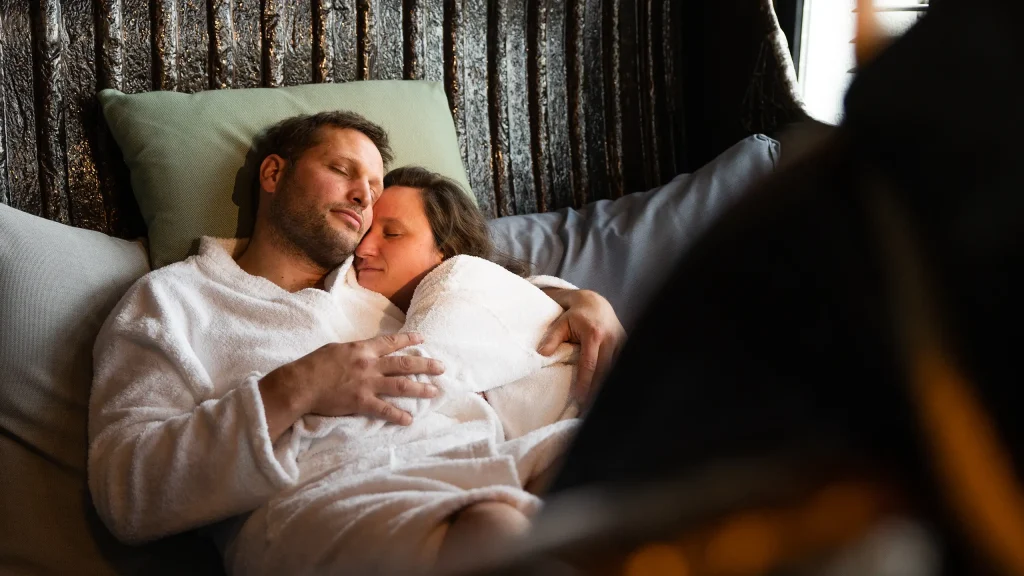 Ein paar bekleidet mit Bademänteln in enger Umarmung liegend in einer schwarzen großen Wanne