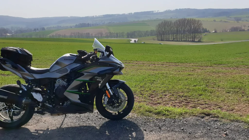 Ein parkendes Motorrad vor einer Landschaft mit Feldern und Wald