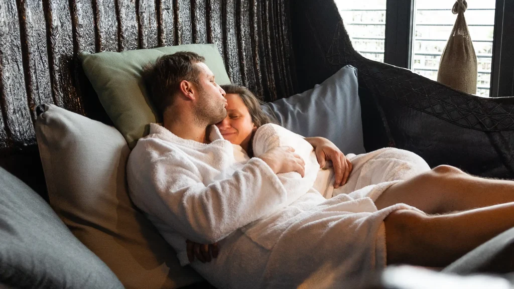 Ein Mann und eine Frau in Bademänteln eng umschlungen in einer großen Wanne liegend