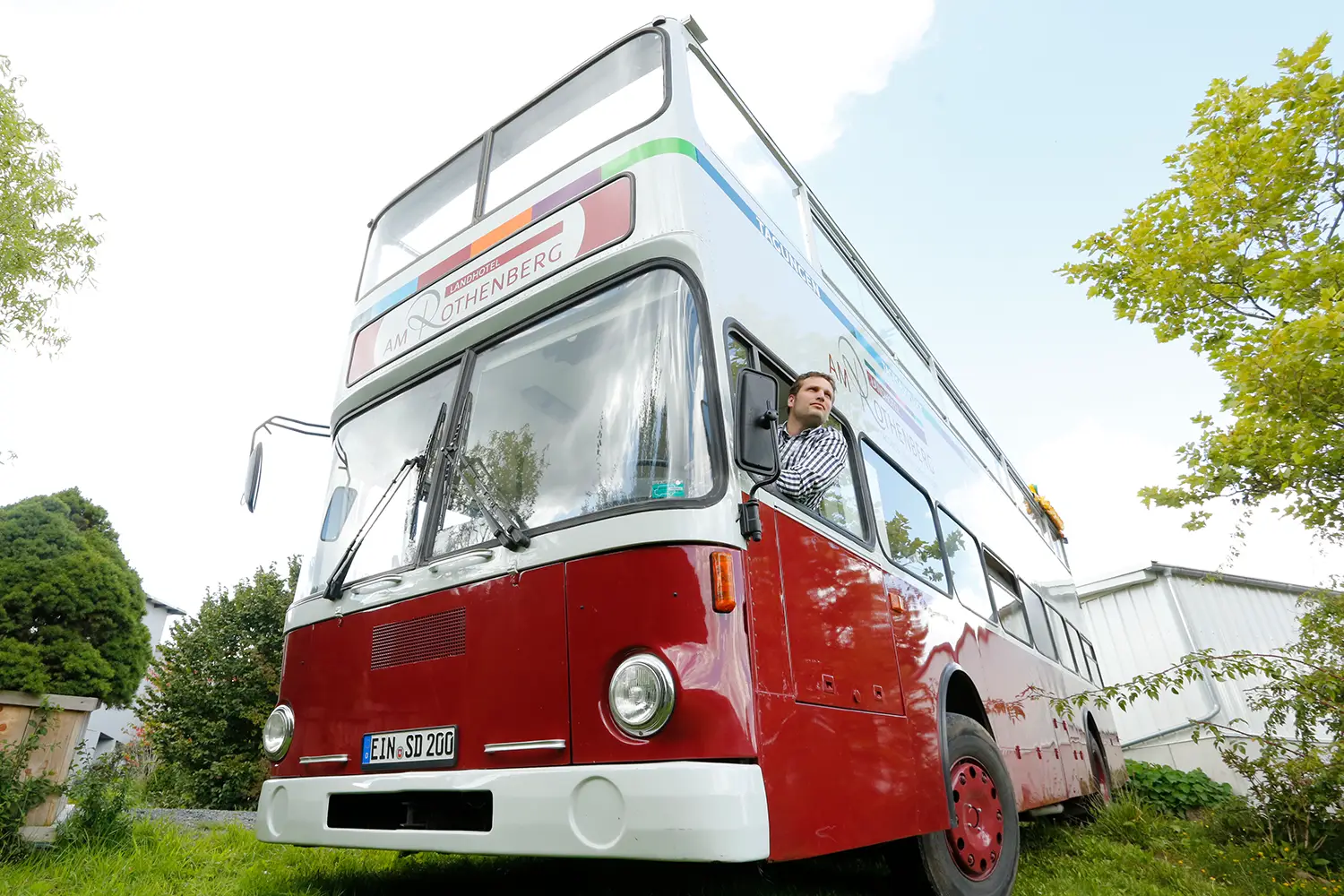 Ein rot-weißer Doppeldecker-Bus aus dem der Fahrer von innen aus dem Fenster schaut