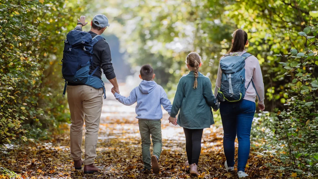 Eine Familie mit zwei Kindern spaziert Hand in Hand auf einem Waldweg