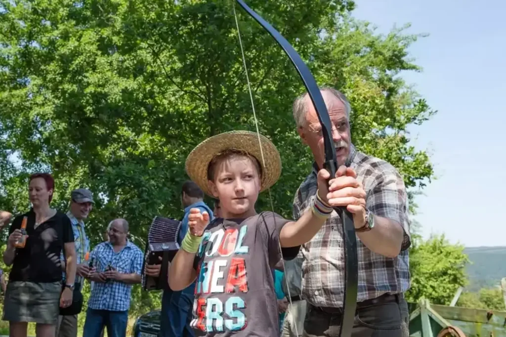 Ein älterer Mann zeigt einem Jungen, wie man mit Pfeil und Bogen schiesst