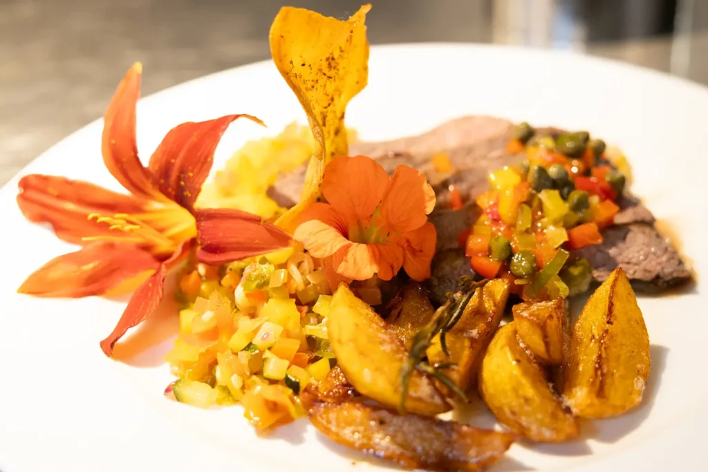 Ein mit Blüten angerichteter Teller mit Fleisch, Gemüse und Kartoffelspalten
