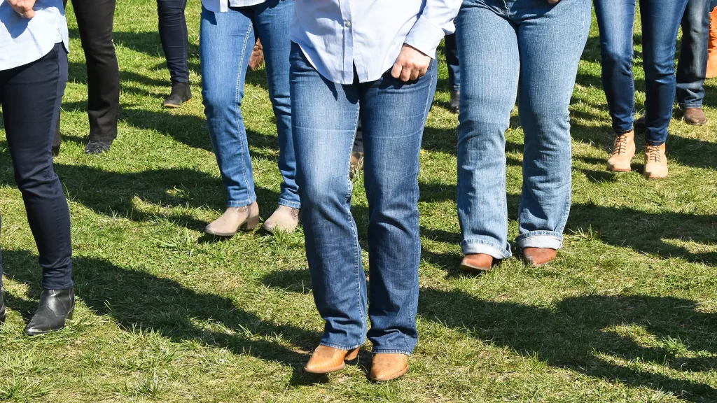 Tanzende Menschen in Jeans und mit Cowboy-Stiefeln auf einer grünen Wiese