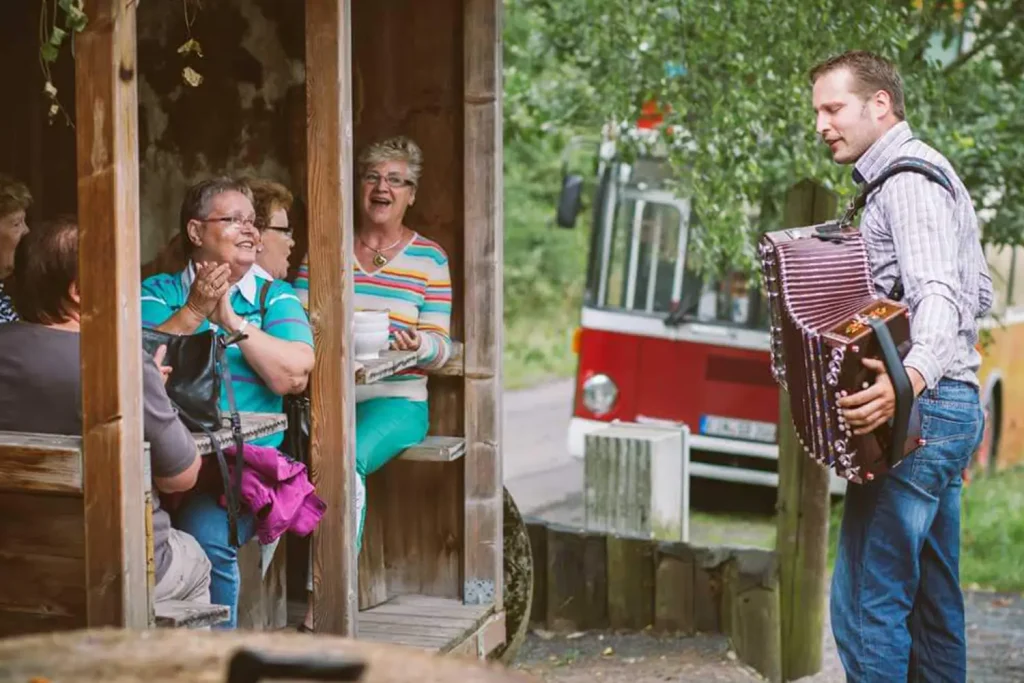 Ein Mann spielt für eine Gruppe Akkordeon, die in einer Hütte sitzt