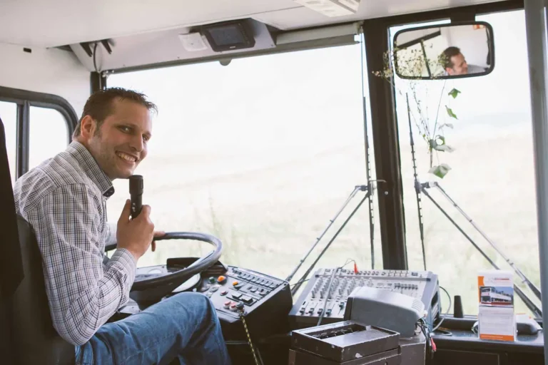 Ein Busfahrer am Steuer mit einem Mikrofon in der Hand